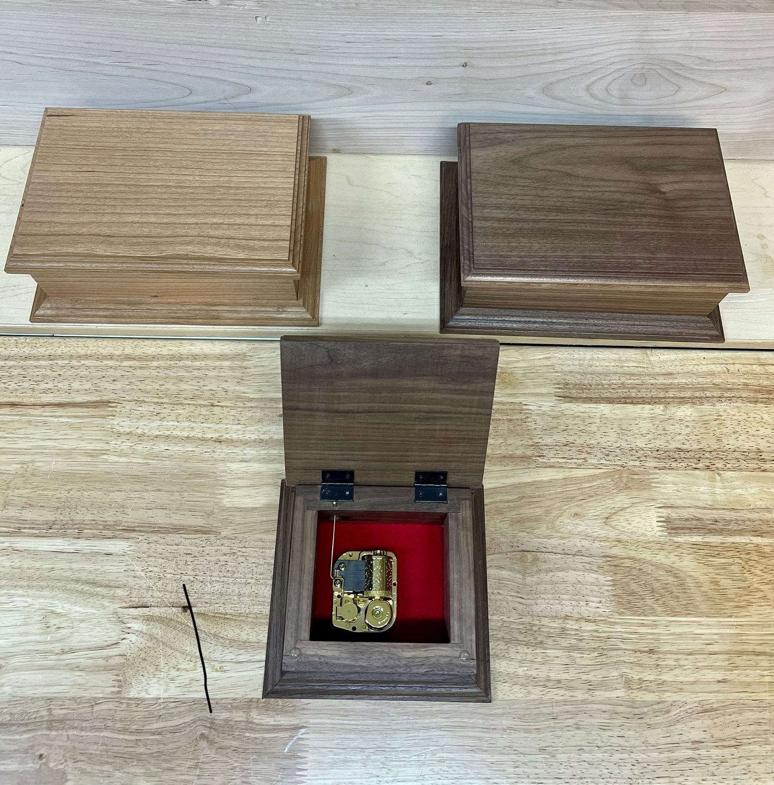 Wooden box with sliding lids revealing a small red compartment holding a gold object.