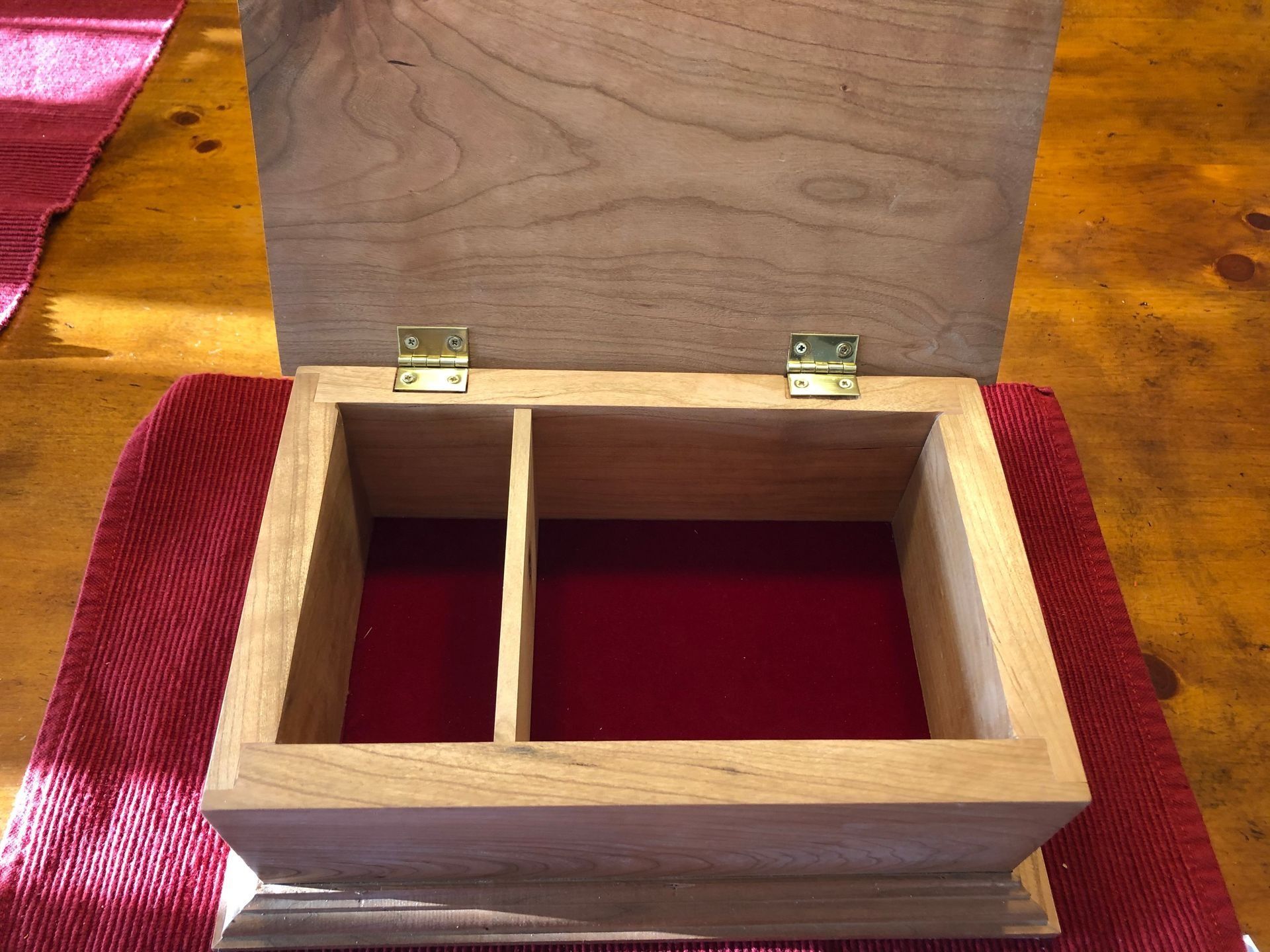 Open wooden box with hinged lid and divided interior on a red tablecloth.