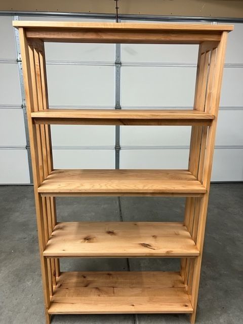 Wooden open shelving unit with four shelves against a gray garage door background