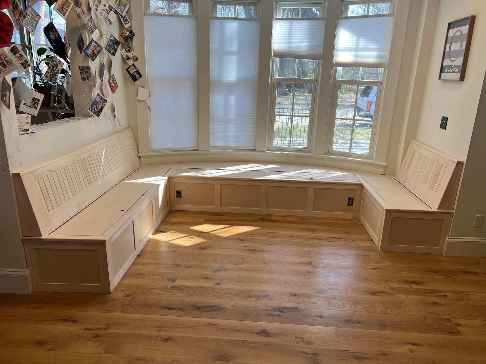 Cozy window seat nook with white built-in benches and warm wood floor in a sunlit room