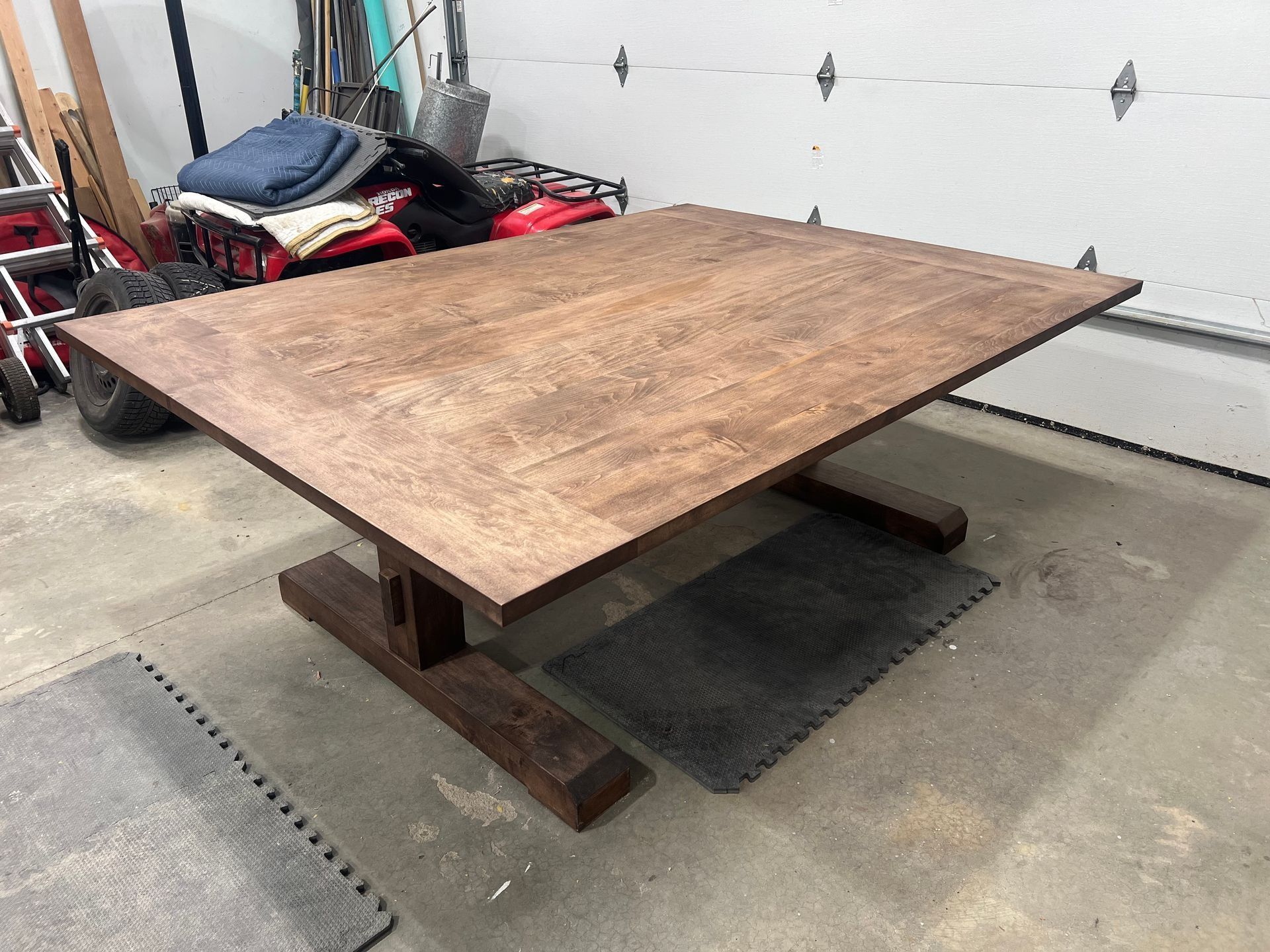 Large wooden worktable on a low metal base in a garage, with tools and equipment in the background.
