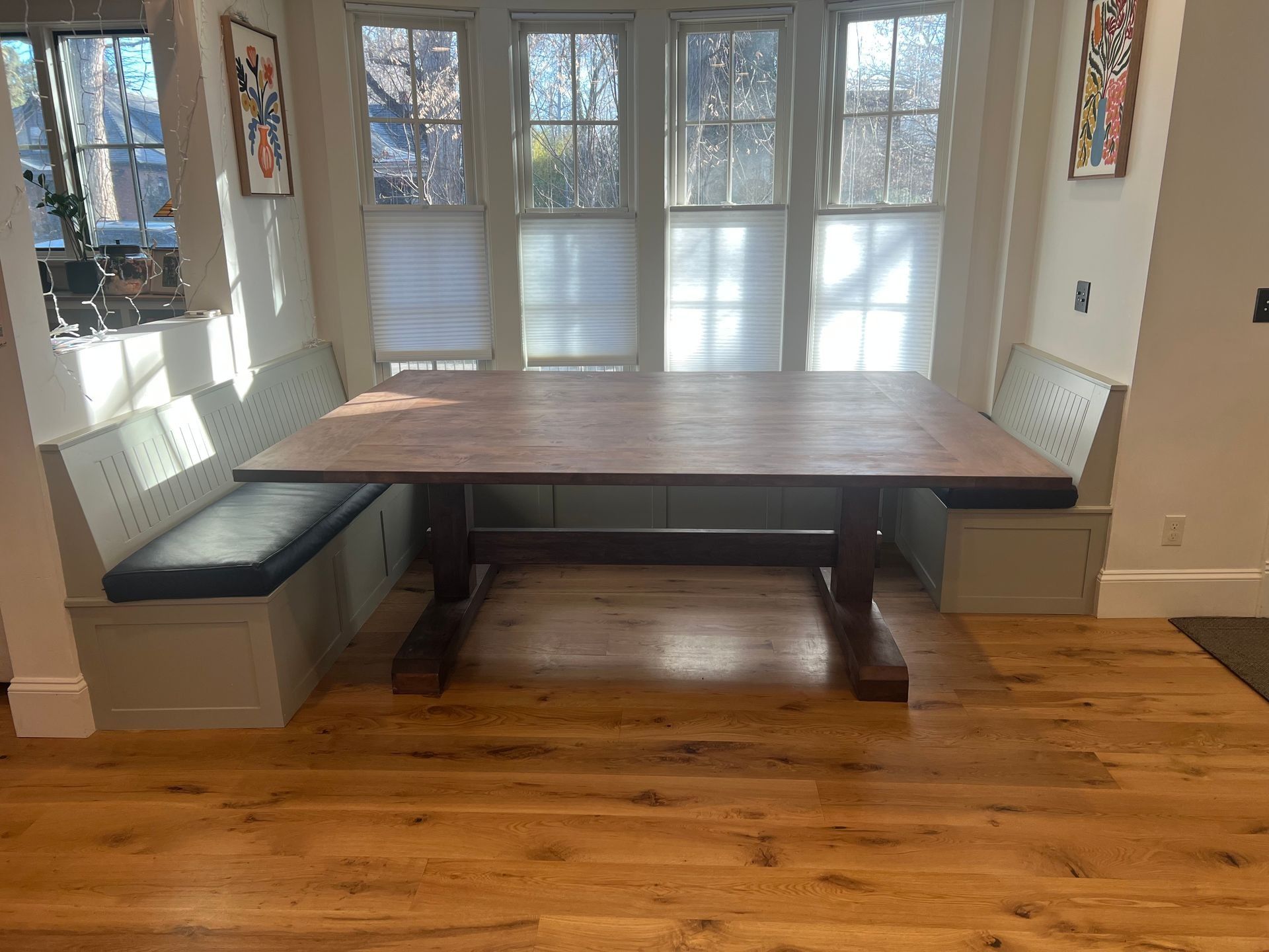 Dining nook with a rectangular wooden table, built-in bench seat, and bright windows in the background