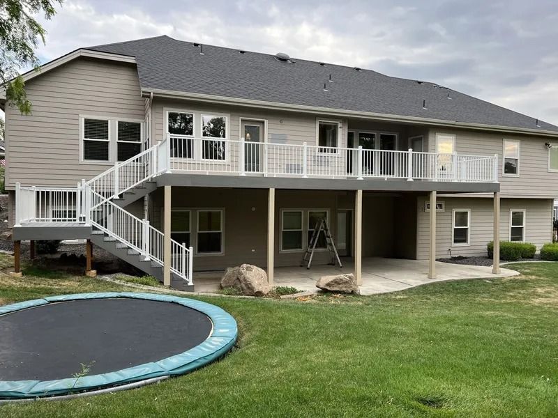 Backyard with raised deck, stairs, covered patio, and a trampoline on the lawn