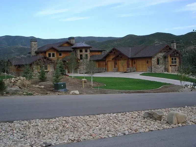 Luxury mountain lodge with wooden cabins, stone accents, and a paved drive under a blue sky.