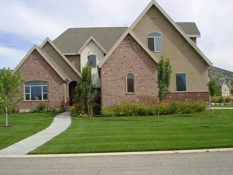 Brick suburban house with beige gables, arched windows, and a green lawn with curved walkway