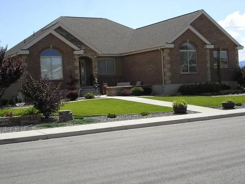 Single-story brick house with a manicured front lawn and driveway along a quiet street