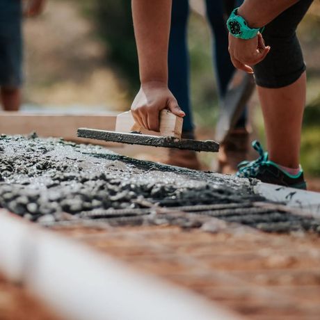 A person is using a trowel to spread concrete on the ground.
