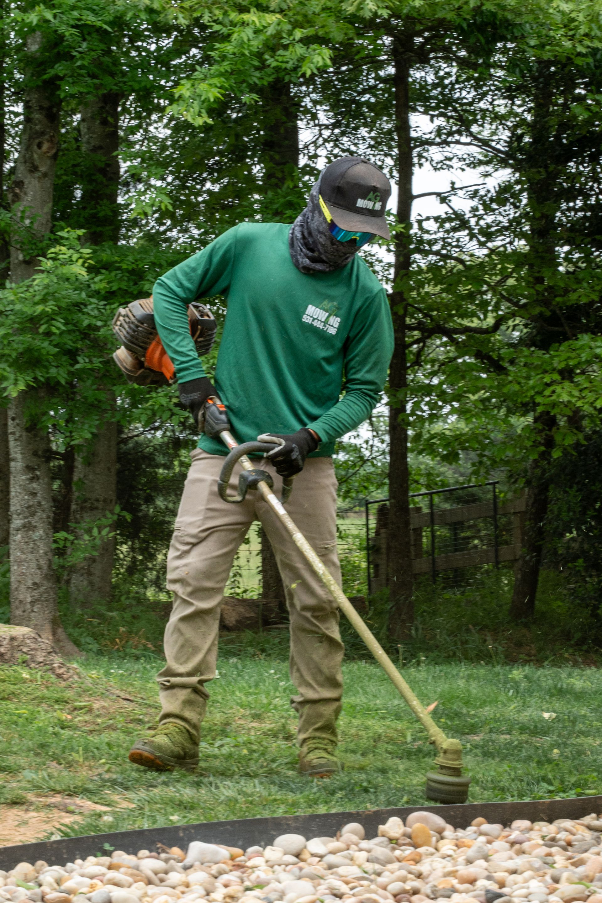 Worker trimming grass along a landscaped edge in a green yard with trees in the background