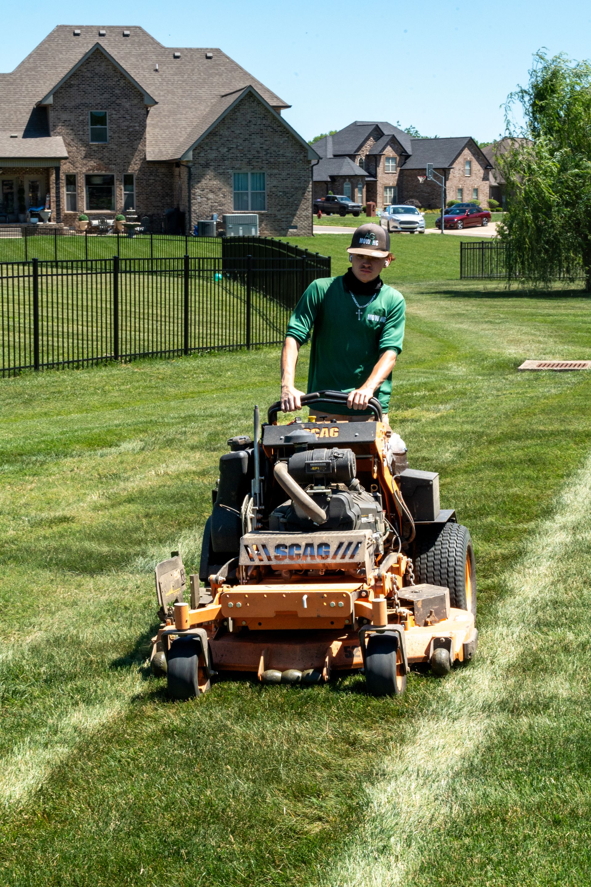 Person mowing a green lawn with a riding mower in a suburban yard