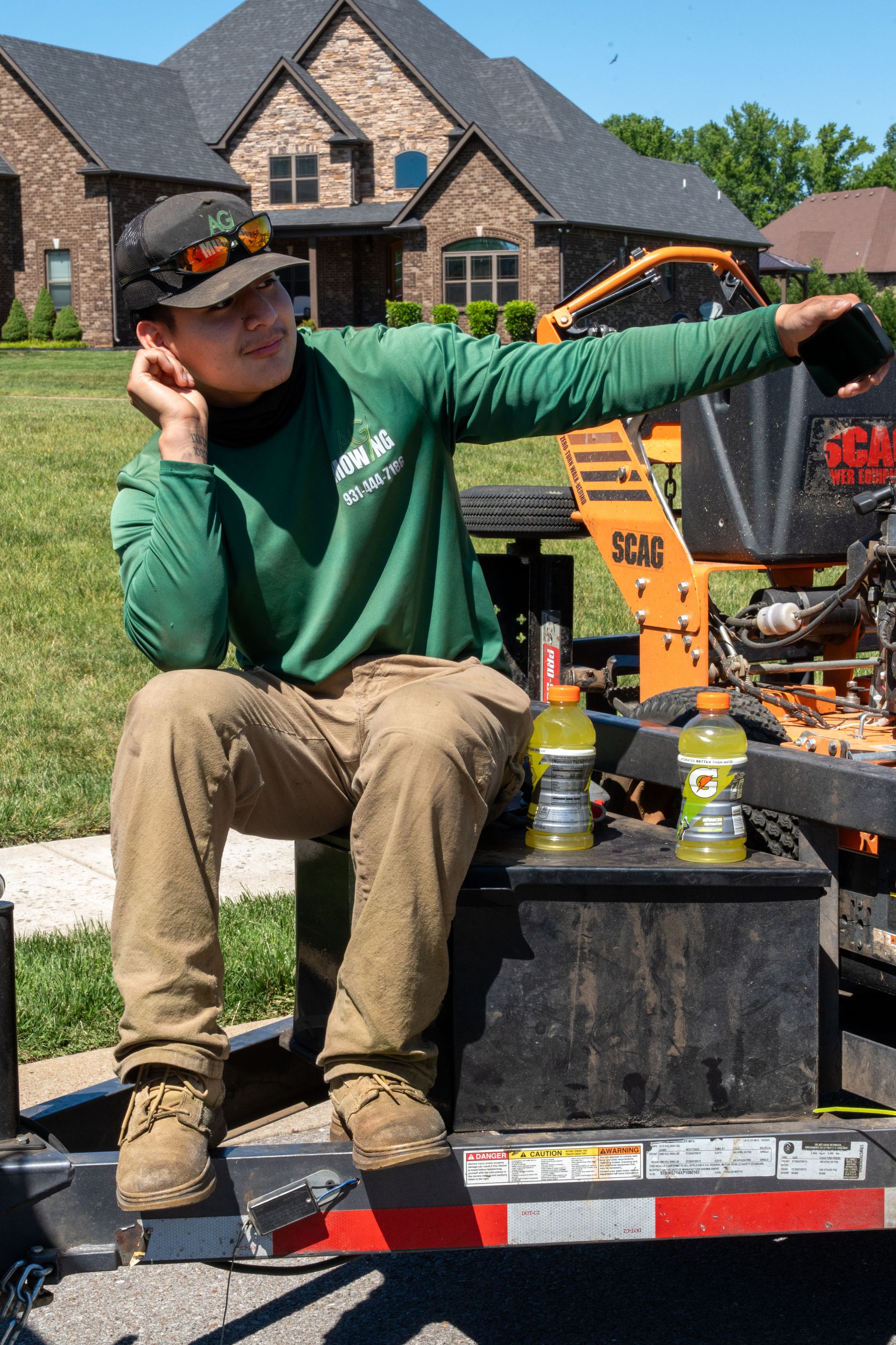 Person in a green shirt sits on a trailer beside a fire pit, pointing outdoors on a sunny day.