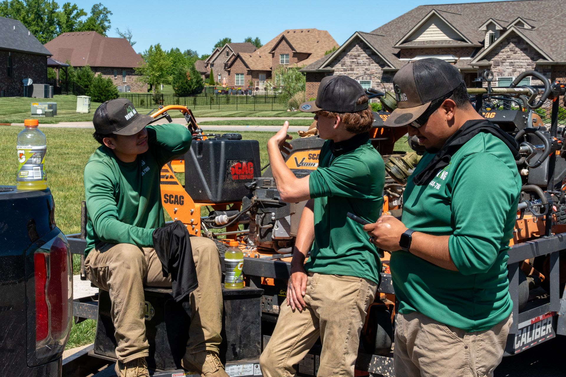 Workers in green shirts inspect equipment at a suburban driveway during a neighborhood cleanup.