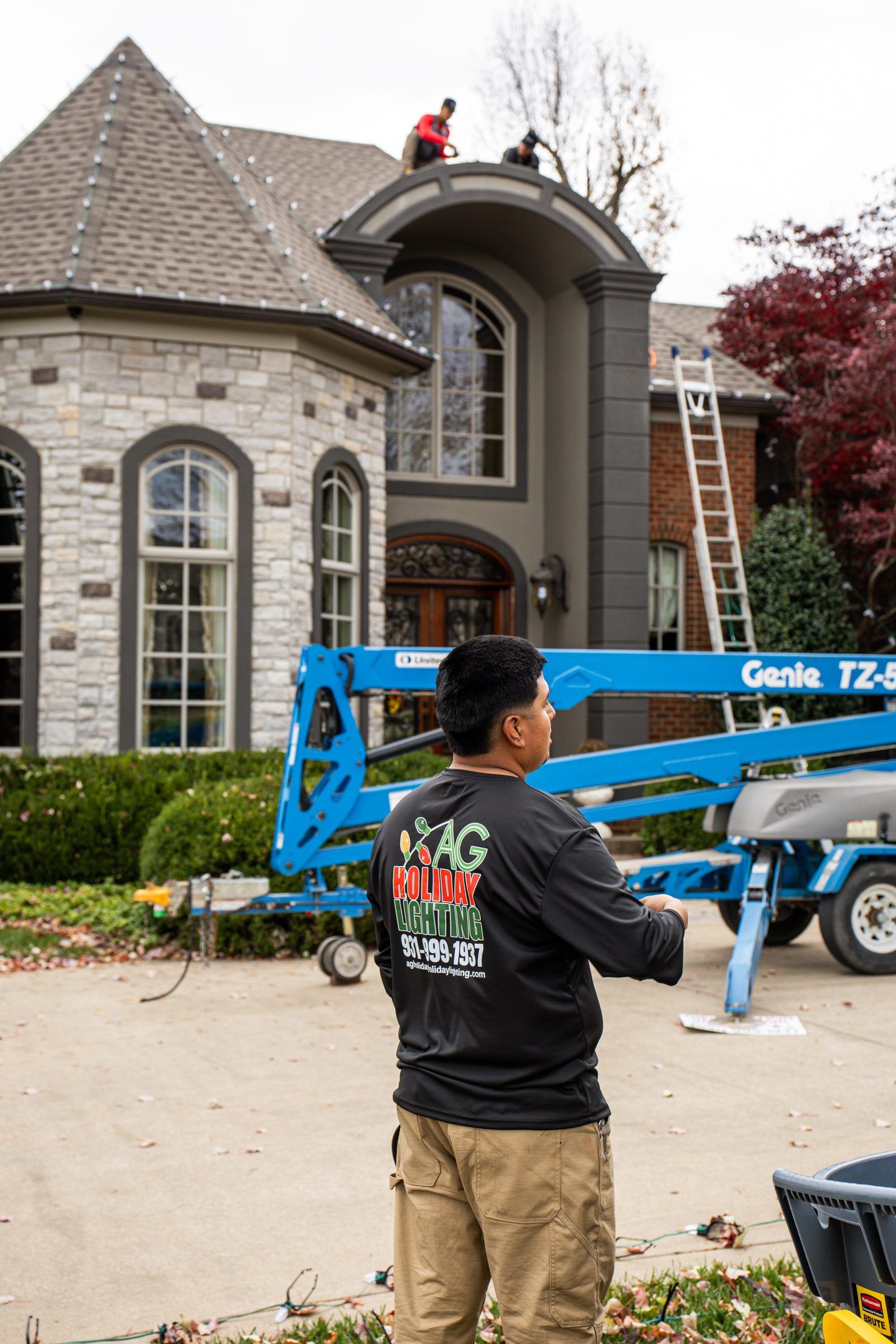 Man observing workers on a lift platform painting a large house exterior.