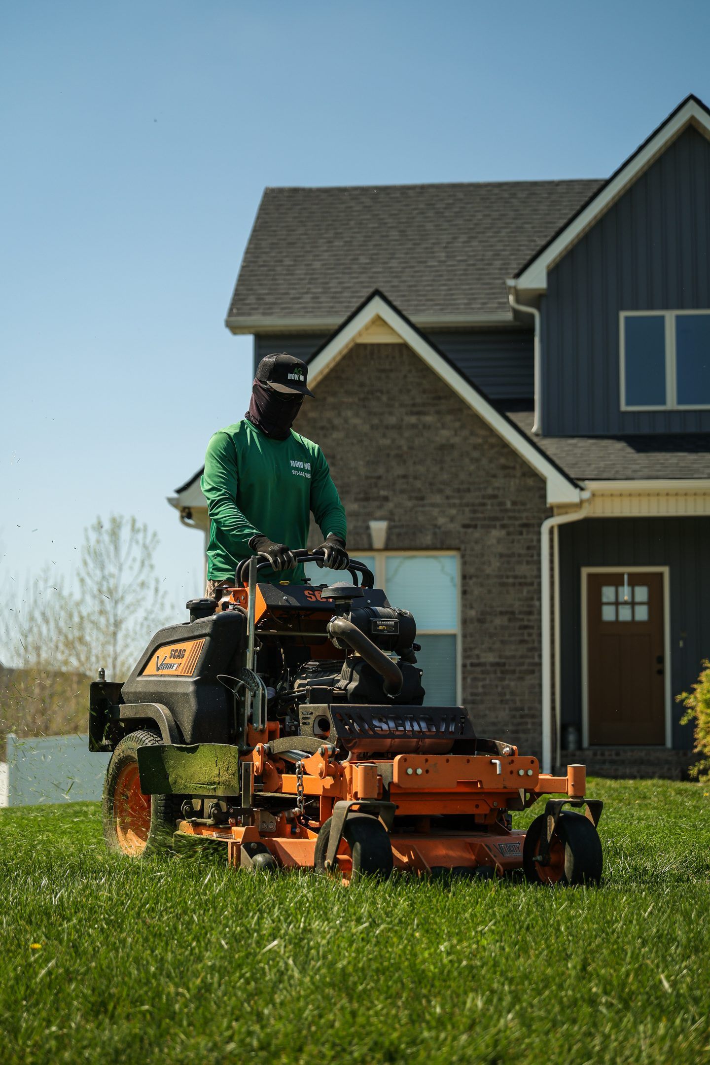 Person mowing a lawn with an orange riding mower in front of a suburban house.