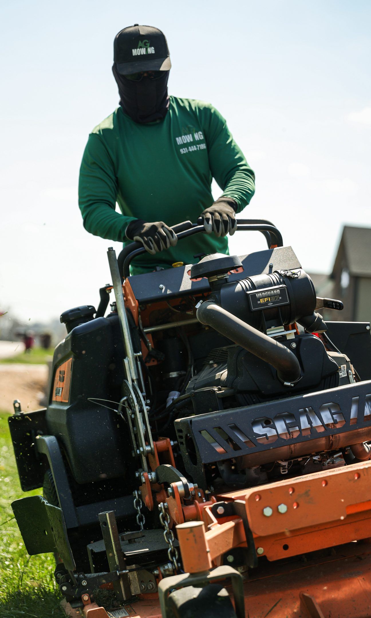Person operating a green and orange lawn mower on a grassy field.
