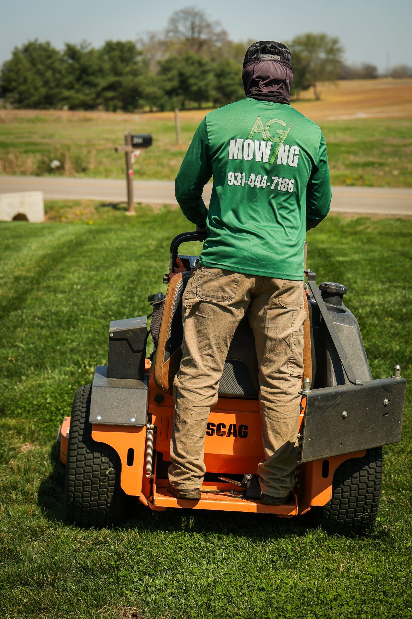 Worker operating an orange lawn mower on a grassy field