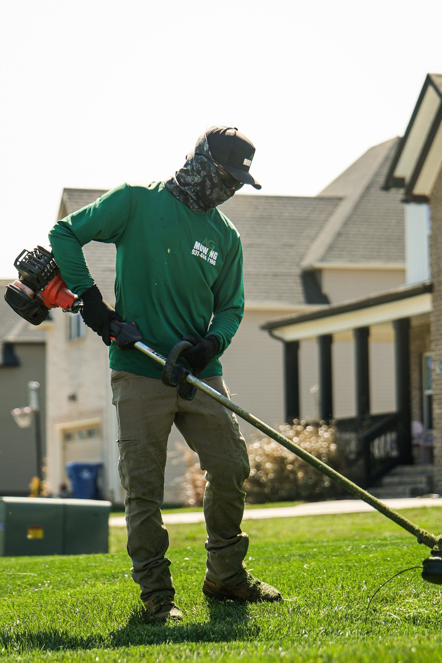 Person using a string trimmer to cut grass on a sunny suburban lawn.