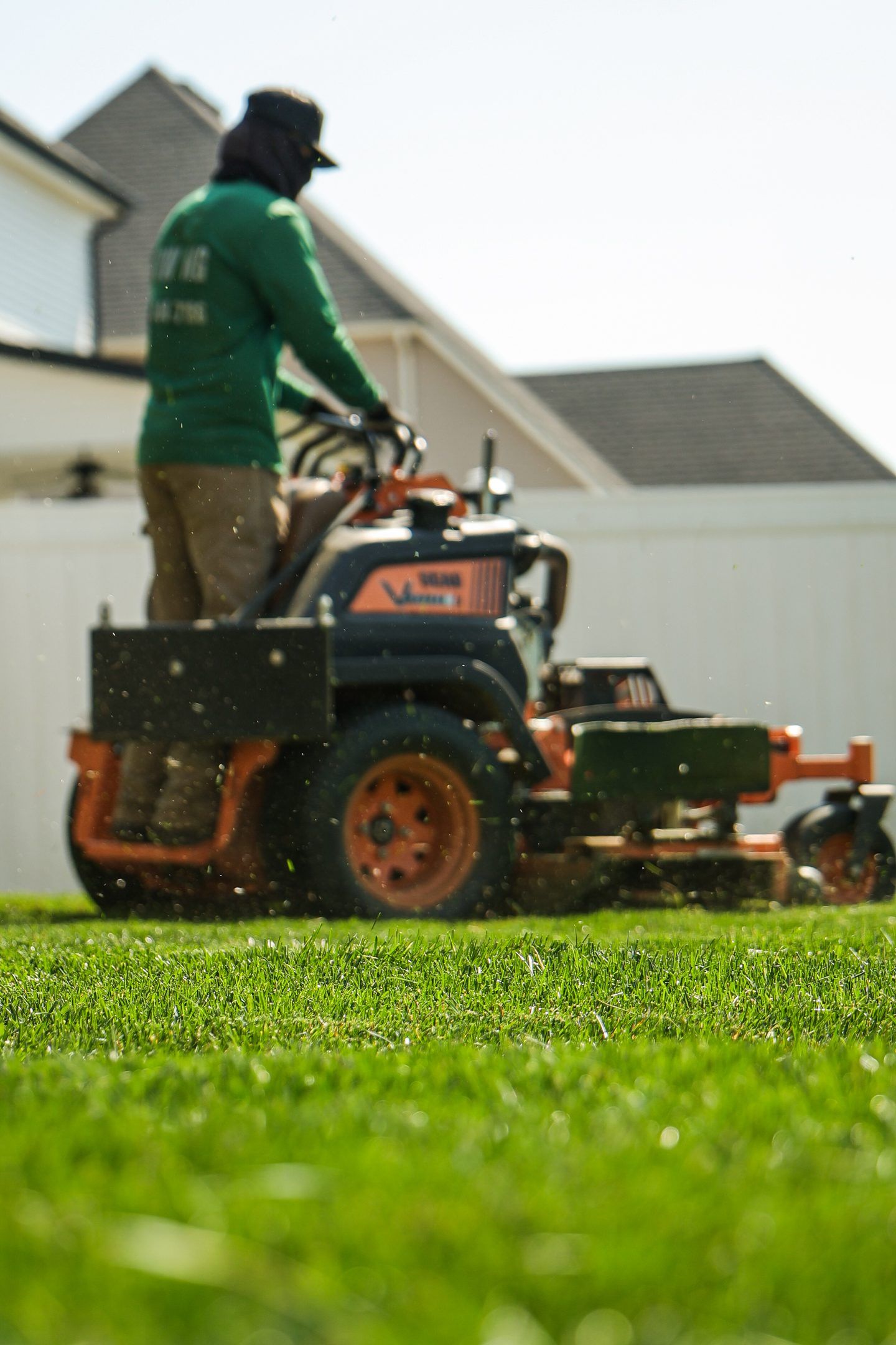 Worker mowing grass on a riding mower in a yard near a white house