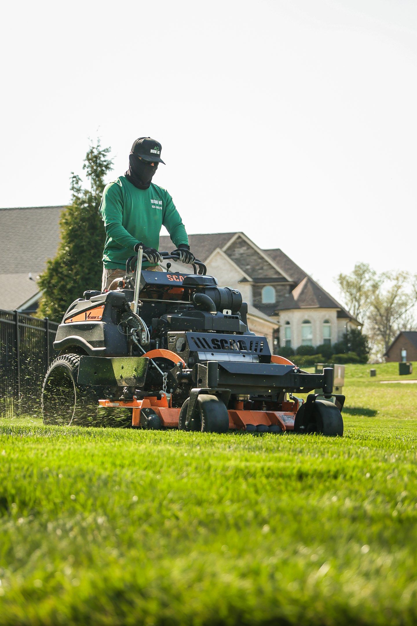 Person operating a lawn mower on a grassy field near houses.