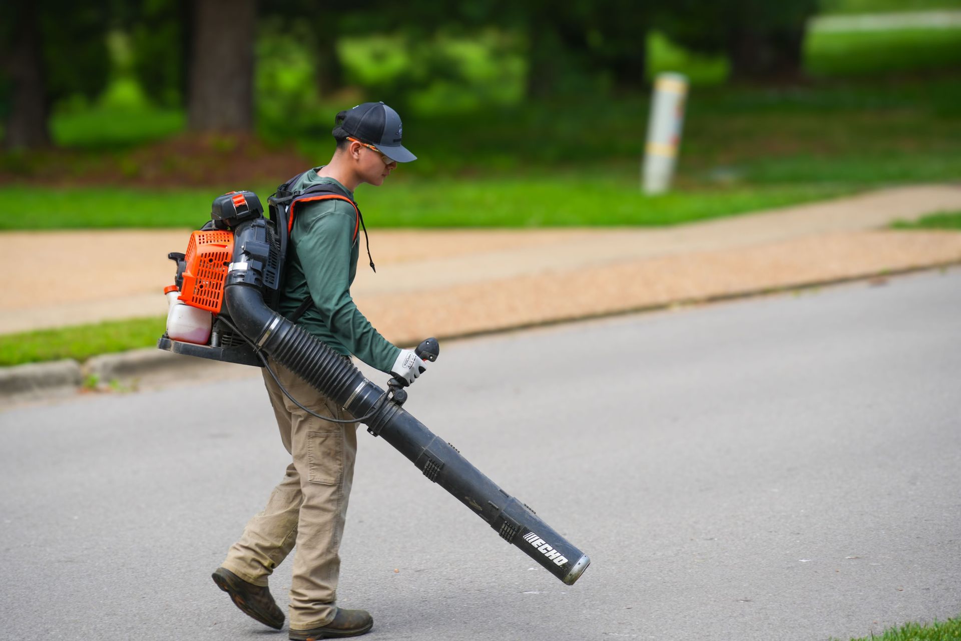 Person wearing backpack leaf blower walks on a paved street.