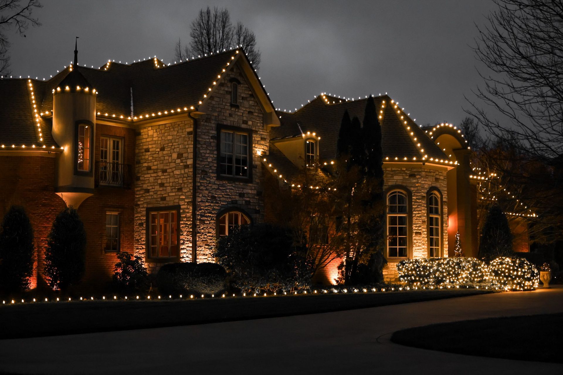 House at night, illuminated with gold Christmas lights along the roof and bushes.