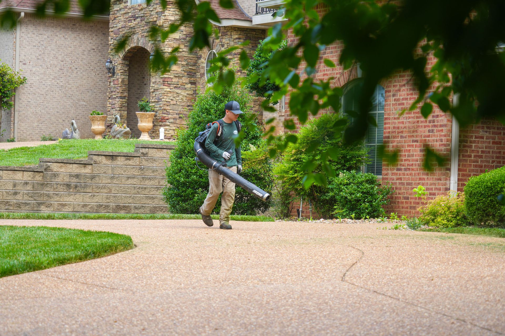 A man is walking down a driveway with a blower in his hand.