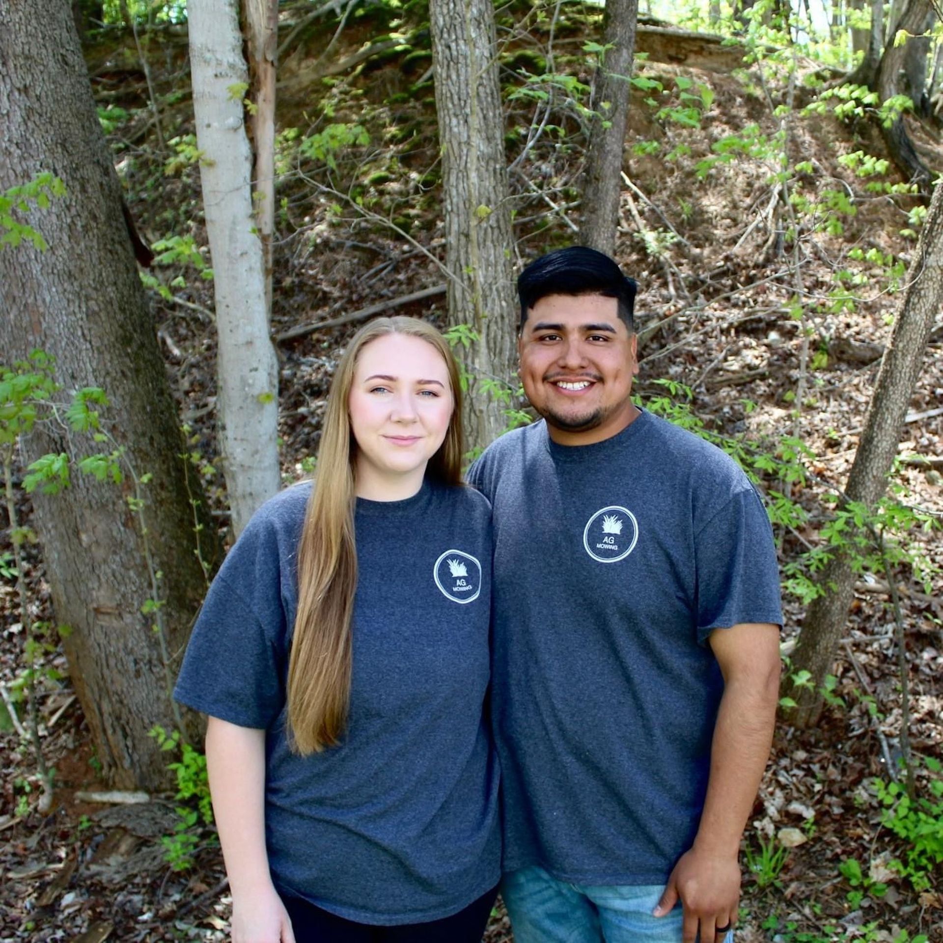 A man and a woman are posing for a picture in the woods.
