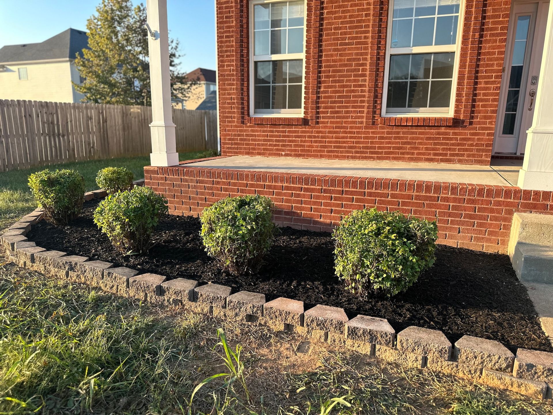 A brick house with a lush green lawn and bushes in front of it.