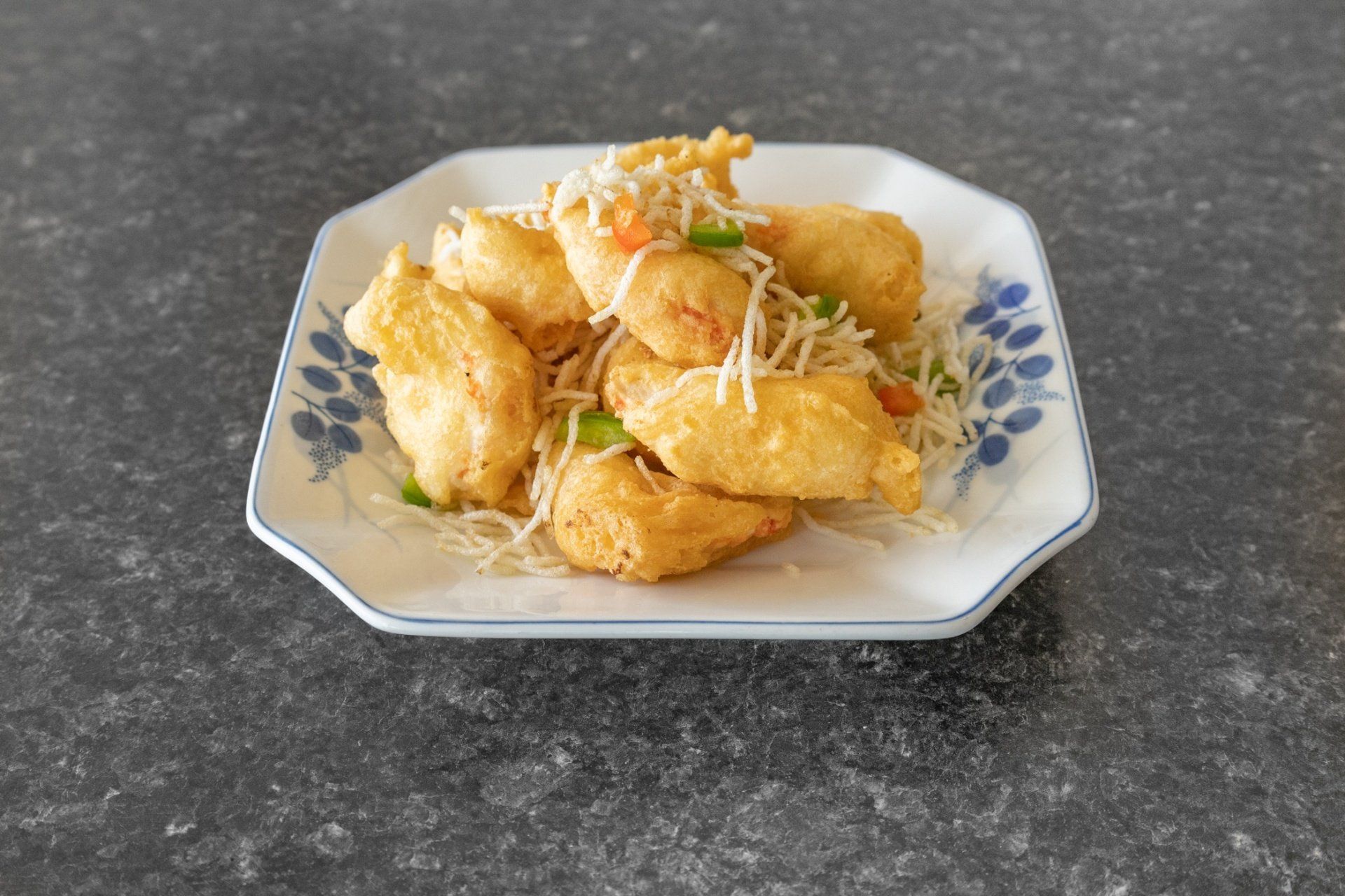 Fried food on a decorative plate, served with shredded garnish on a dark surface.
