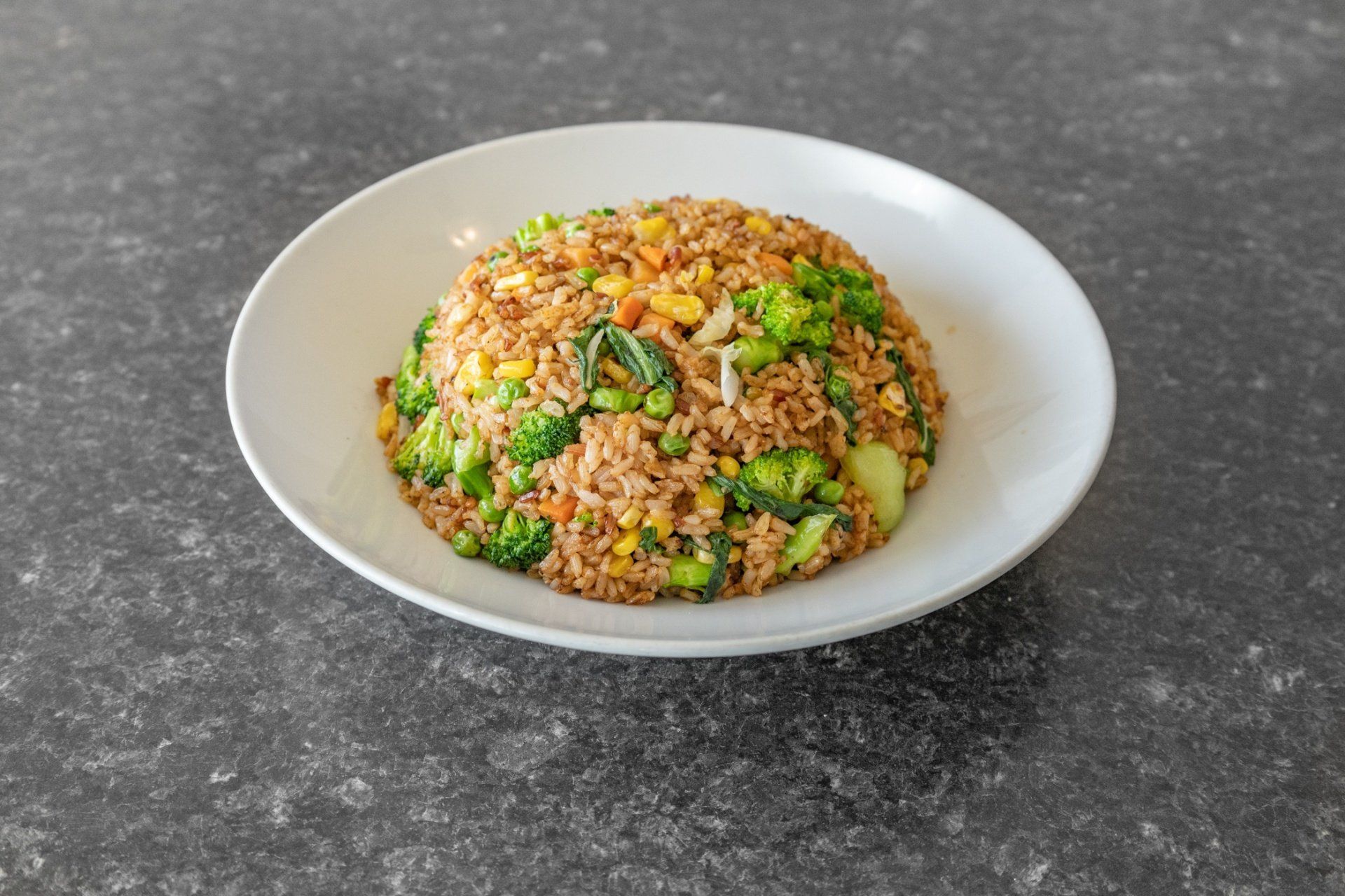 Fried rice with vegetables on a white plate, gray background.