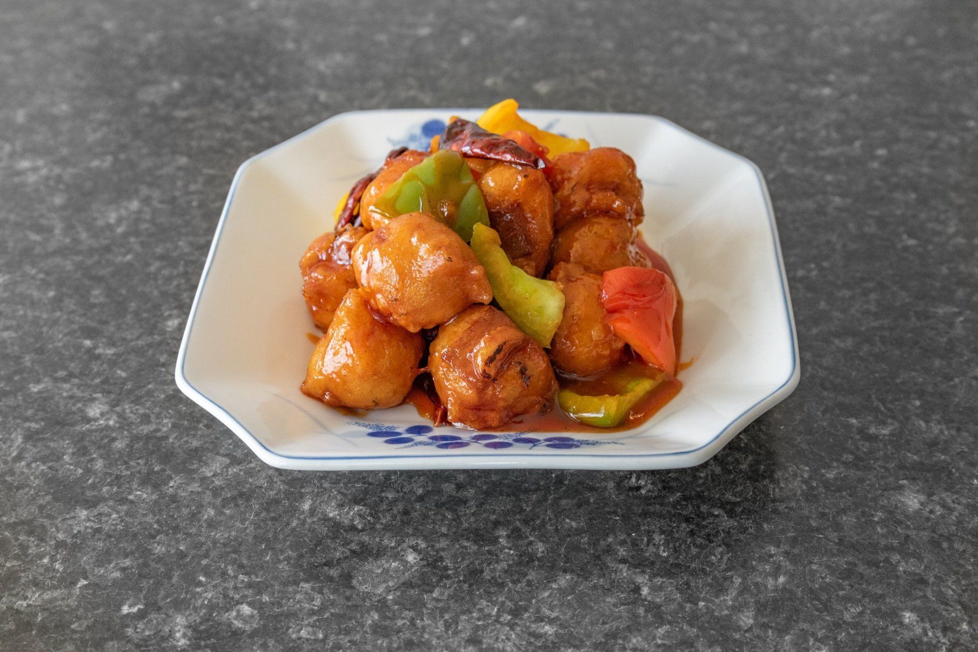 Sweet and sour chicken dish with colorful peppers, served on a white plate with blue floral accents.