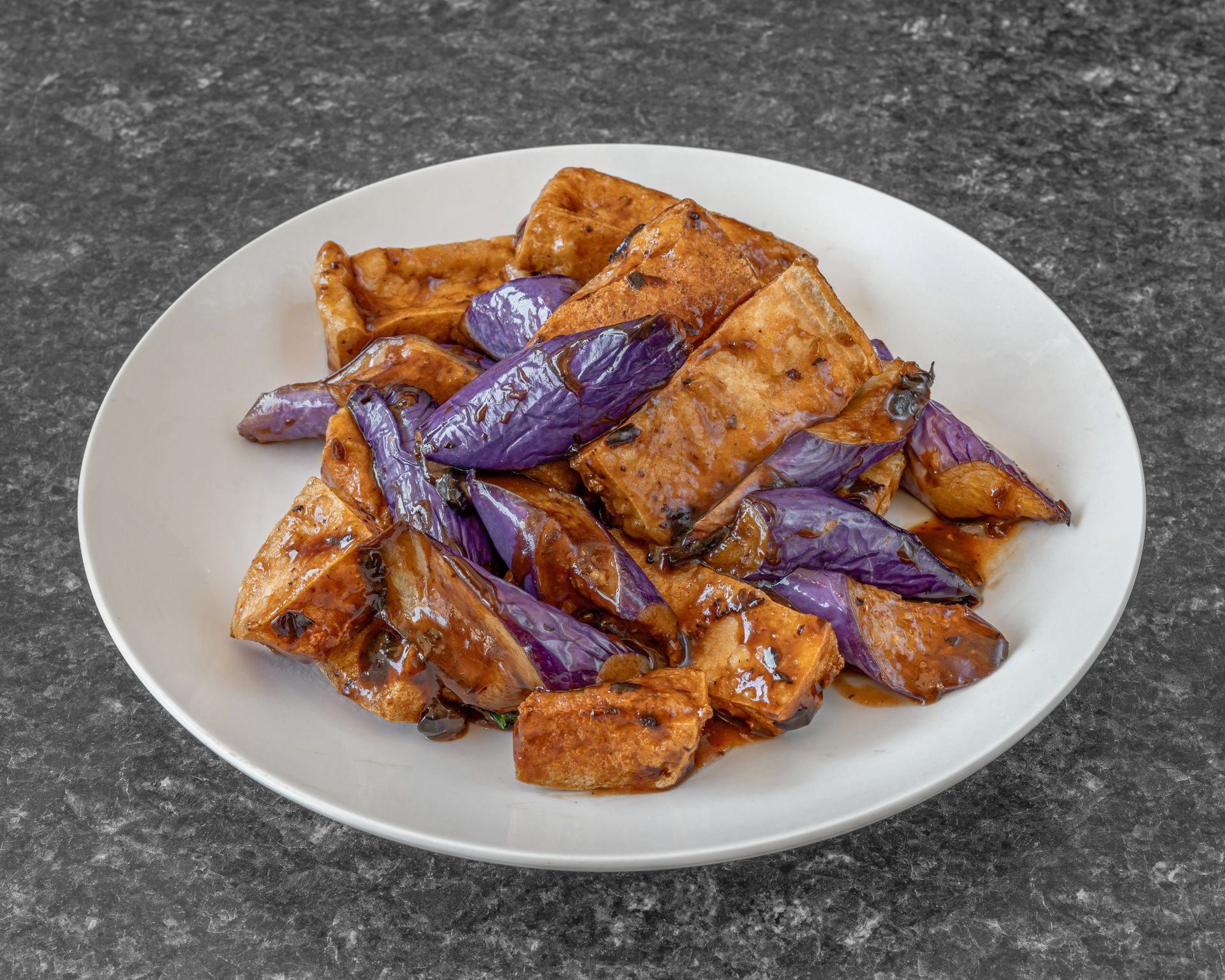 Plate of tofu and purple eggplant in a dark sauce.
