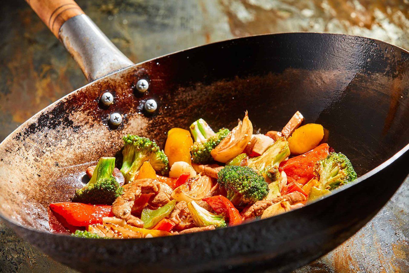 Stir-fry vegetables and chicken cooking in a well-worn wok with a wooden handle.