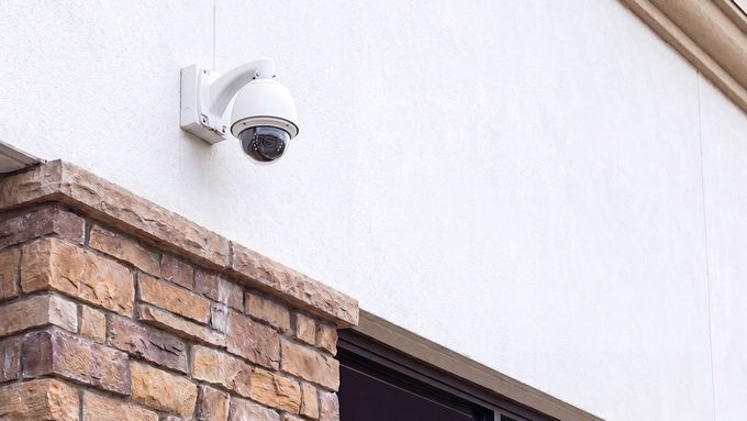 Security camera mounted on a white exterior wall above a brick facade