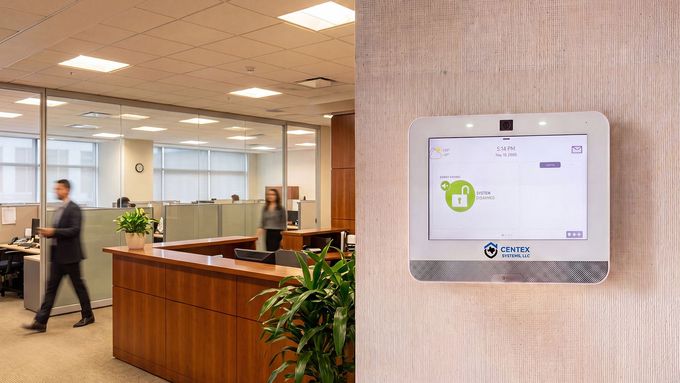 Office lobby with a wall-mounted access control panel and people walking near reception.
