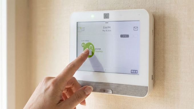 Hand pressing a white wall-mounted touchscreen thermostat in a home hallway