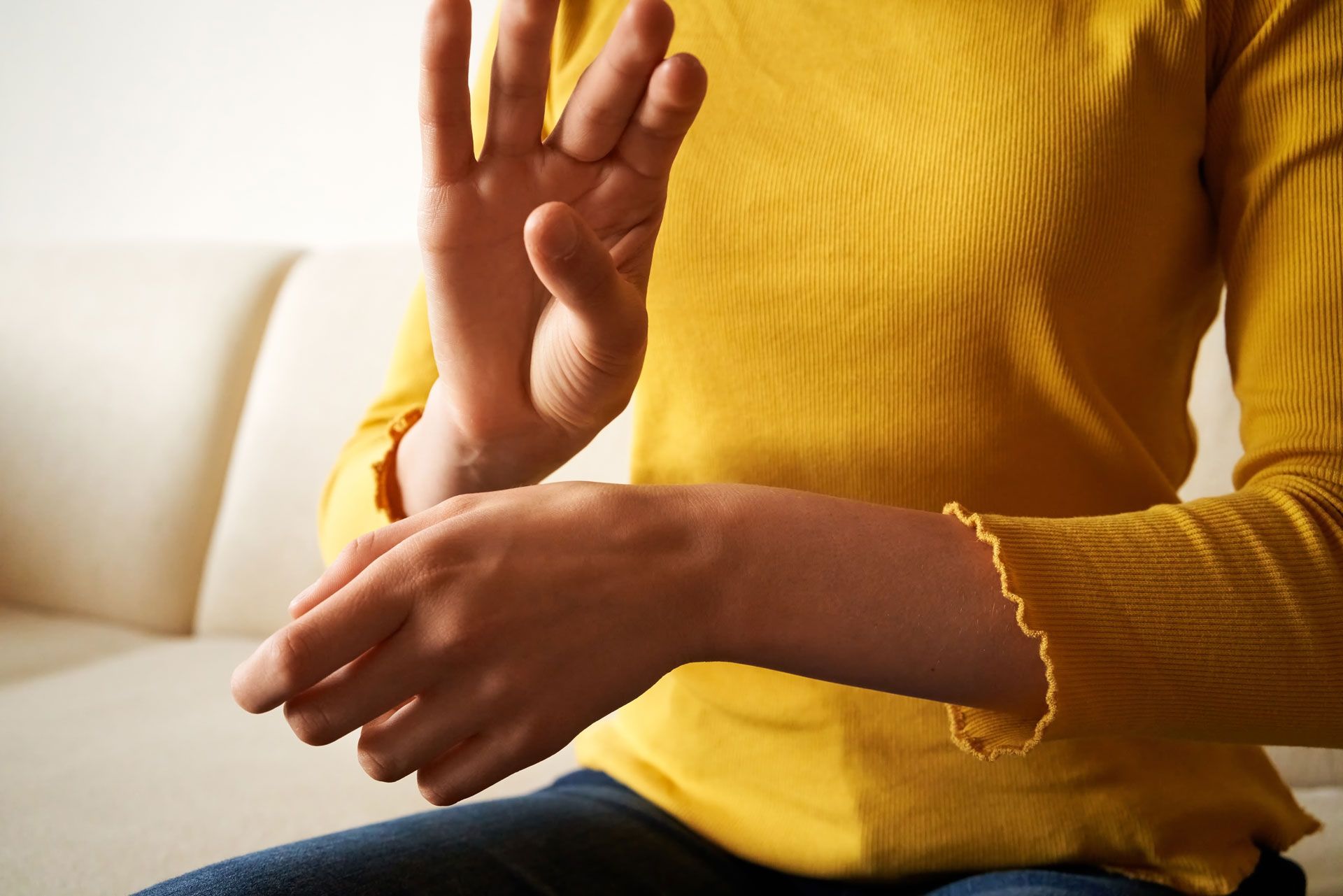 A woman in a yellow shirt is sitting on a couch making a stop sign with her hands.