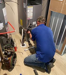 Technician kneeling beside a furnace, working on HVAC equipment with tools in a utility room