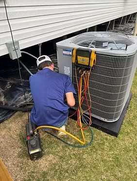 Technician servicing an outdoor HVAC unit with gauges beside a house