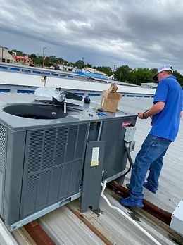 Technician inspecting rooftop HVAC unit beside a waterfront under cloudy skies