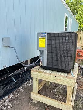 Outdoor HVAC unit on a wooden platform beside a blue building with exposed utility piping.