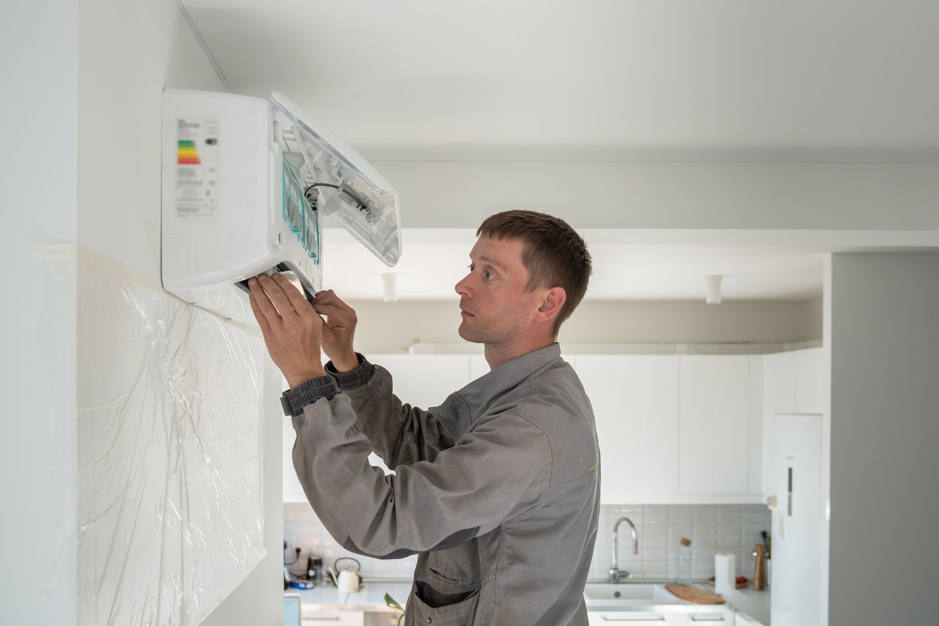Technician repairing a wall-mounted air conditioner in a bright kitchen
