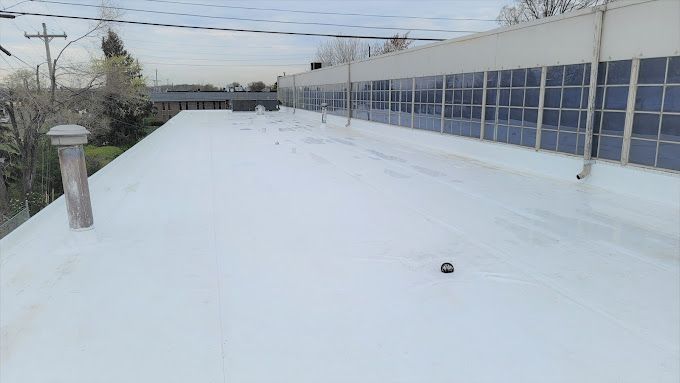 White roof with a small black object on it. A building with windows is to the right.