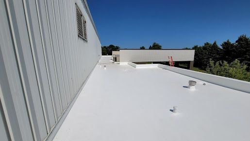 White commercial building roof with a bright blue sky and trees in the background.