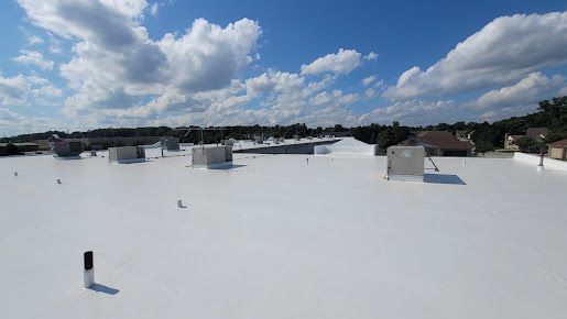 White commercial roof under a blue sky with scattered clouds, buildings and trees in background.