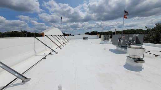White commercial roof on a sunny day, with equipment and a flagpole against a cloudy sky.