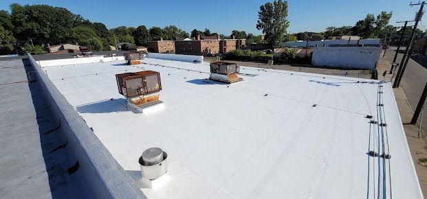 A white commercial roof with several vents and a clear blue sky.