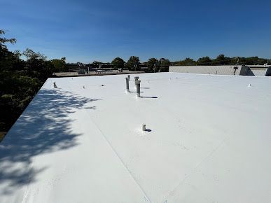 White commercial roof under a clear blue sky; vents and pipes protrude.