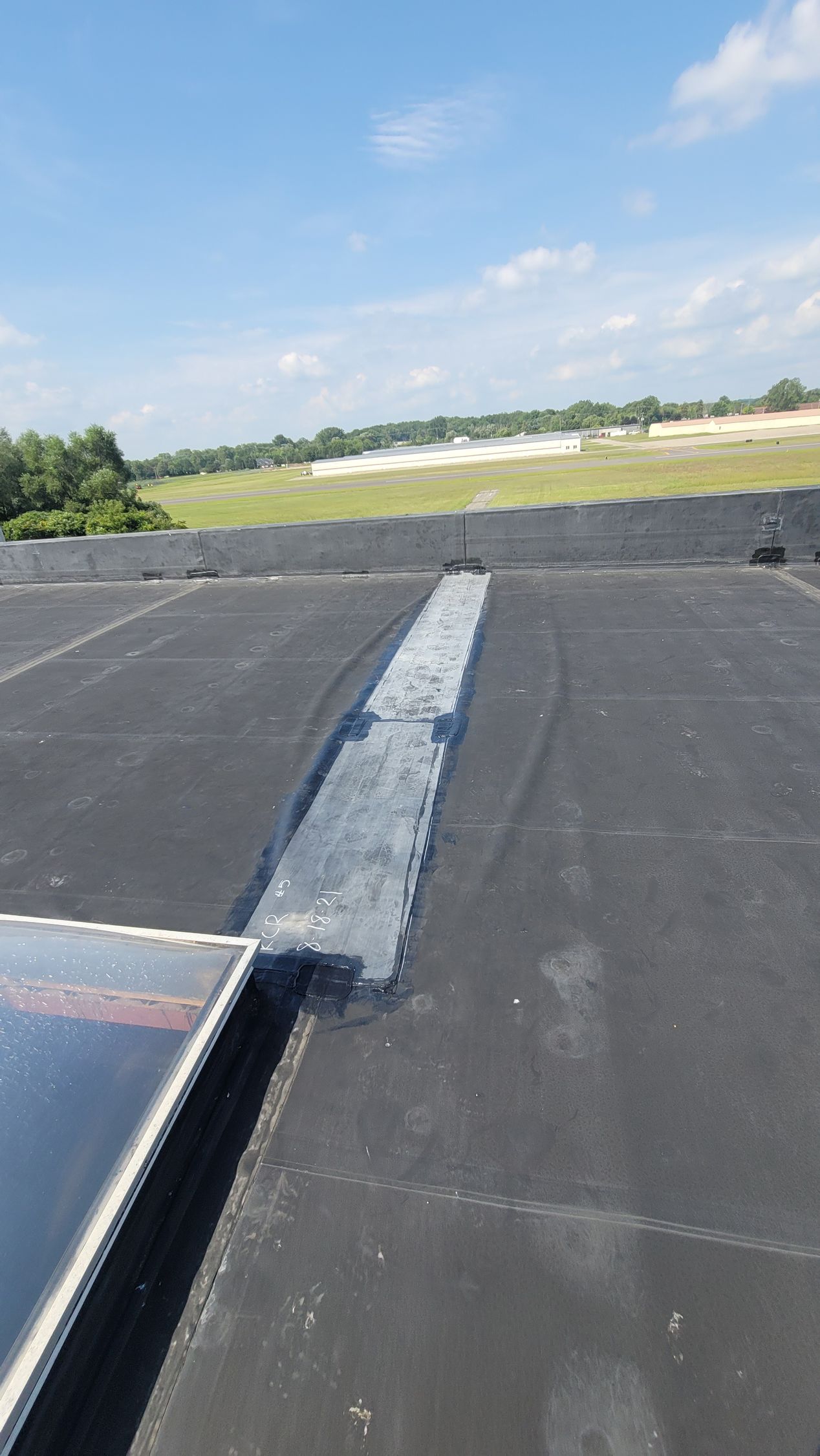 Flat black roof with a repaired seam, sunny day, blue sky, and distant green landscape.