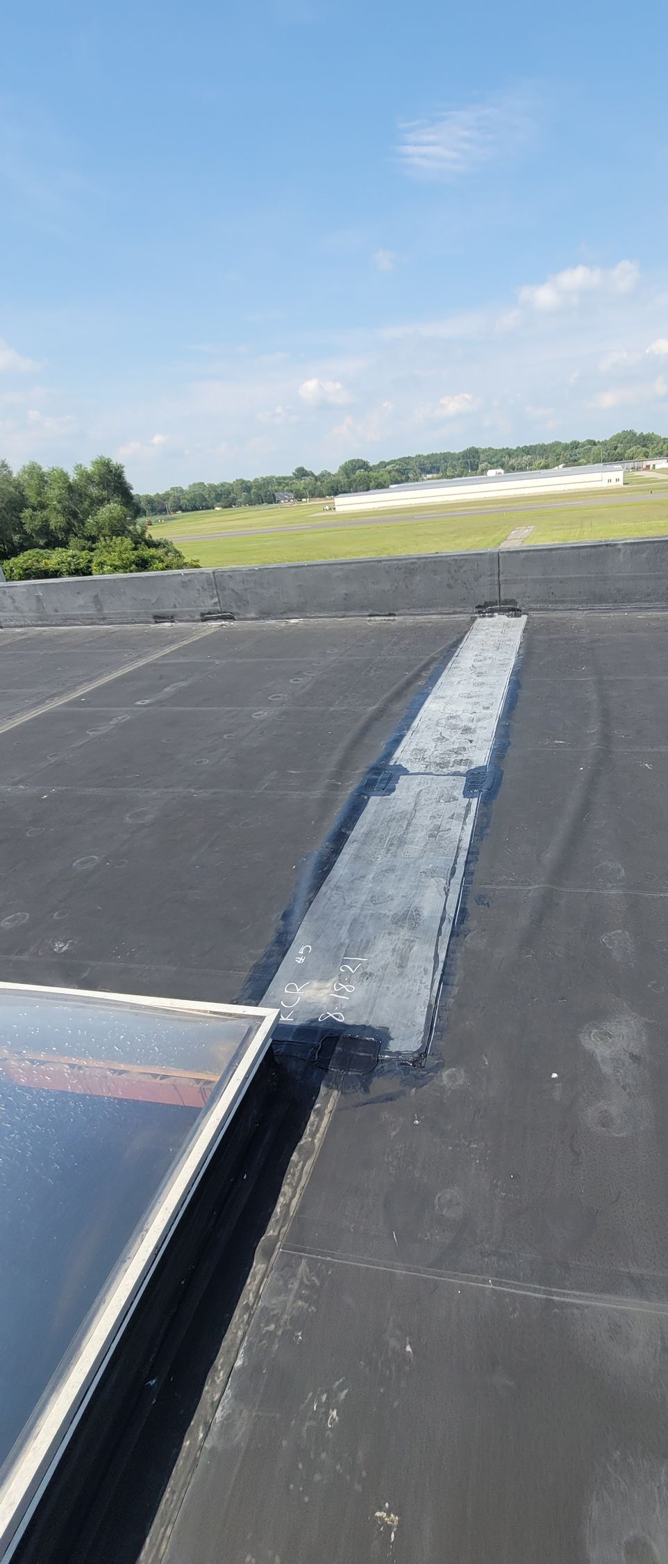View of a black tar roof with a repaired section and a blue sky background.