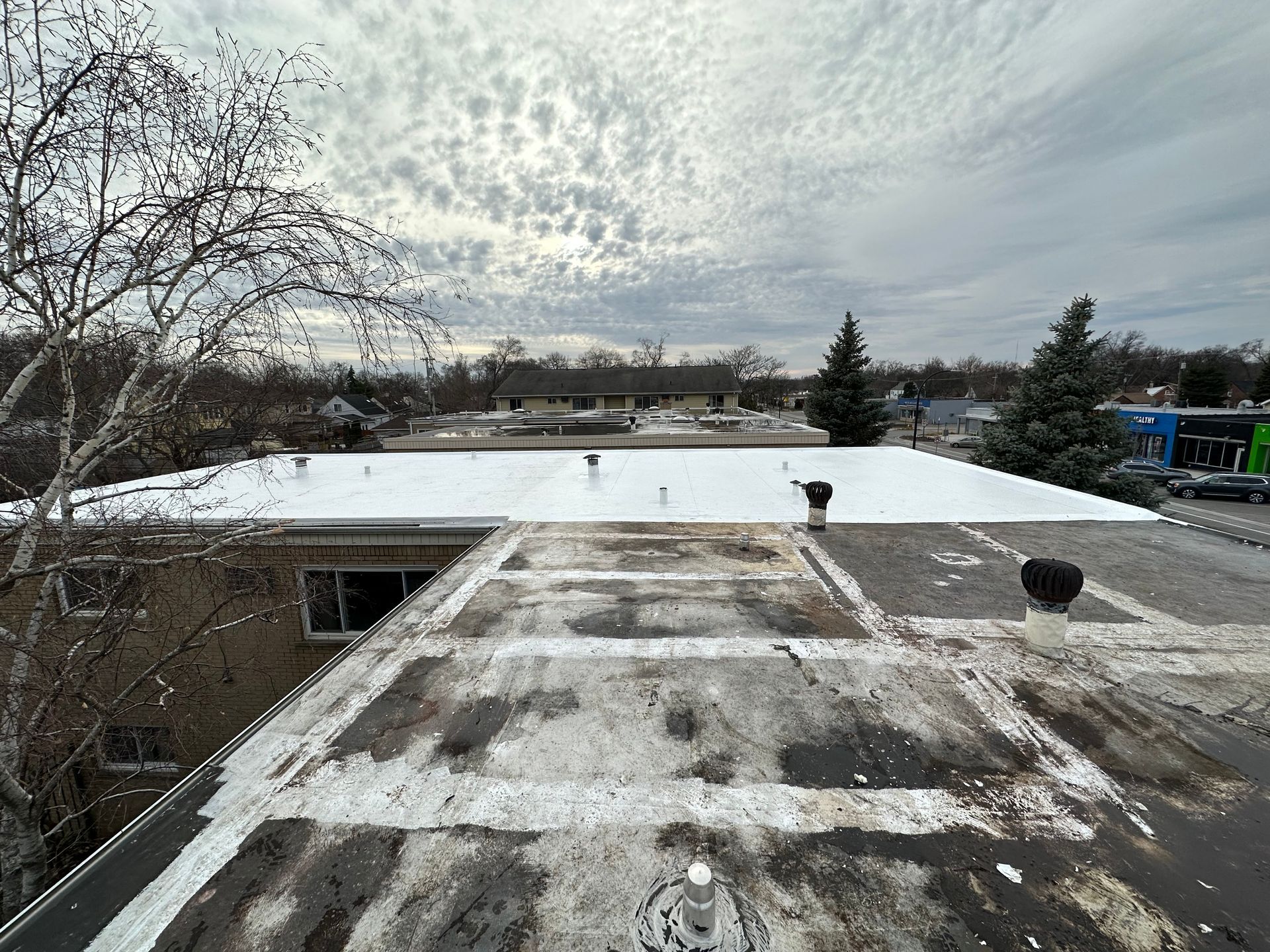 Overhead view of a flat roof with patches of snow, trees, and a cloudy sky in the background.